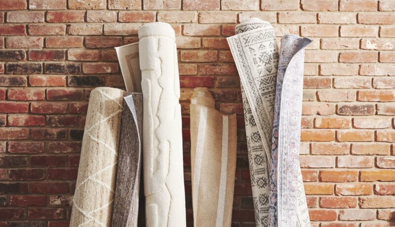 Collection of cream rugs rolled up against a brick wall.