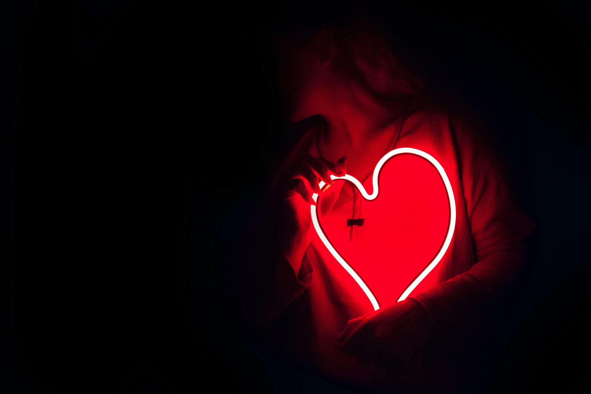 A neon red light up heart being held by a person in the dark