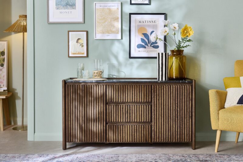 A sideboard and armchair-dining room furniture-vintage patterned rug-mustard armchair-dark wood fluted sideboard-marble top sideboard-gallery wall-stylish vases-glassware