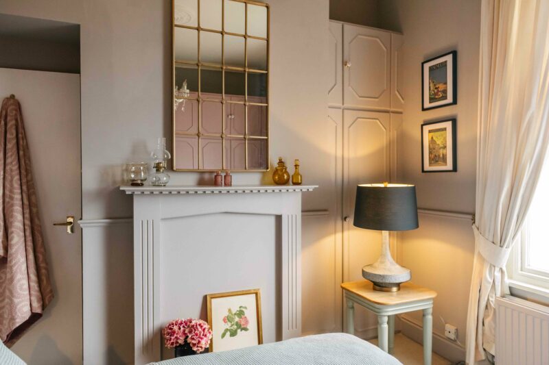 A mirror, fireplace, side table and lamp-bedroom furniture-antique gold grid mirror-painted fireplace-warm neutral walls-painted side table with wooden top