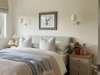 A bed and bedside table-bedroom furniture-neutral walls-upholstered bed-layered bedding-painted wooden bedside table-sheepskin rug-statement ceiling light-delicate wall lights-fresh flowers-natural light