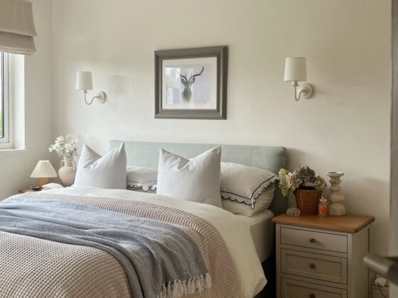 A bed and bedside table-bedroom furniture-neutral walls-upholstered bed-layered bedding-painted wooden bedside table-sheepskin rug-statement ceiling light-delicate wall lights-fresh flowers-natural light
