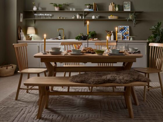 A dining table, display cabinet and bench-kitchen diner furniture-oak dining table set-neutral textured rug-spindle back chairs-olive green walls-sheepskin rug-tapered candles-soup bowls-bistro curtain-grey kitchen-open kitchen shelving-brass tap-autumnal tablescape