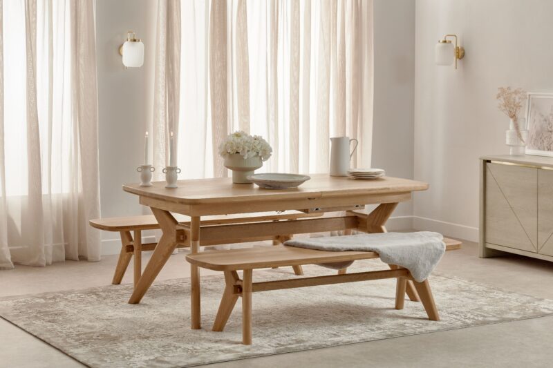 A dining table-dining room furniture-oak dining table and benches-neutral walls-sheer curtains-neutral rug-faux sheepskin rug-off white ceramics-wall lights