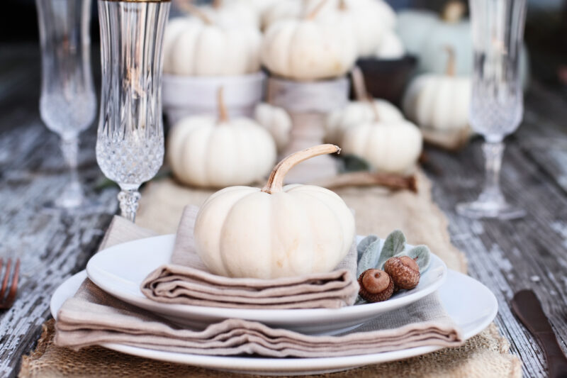 A dining table-dining room furniture-white pumpkins-champagne glasses-white crockery-hessian table runner-neutral napkins-rustic dining table