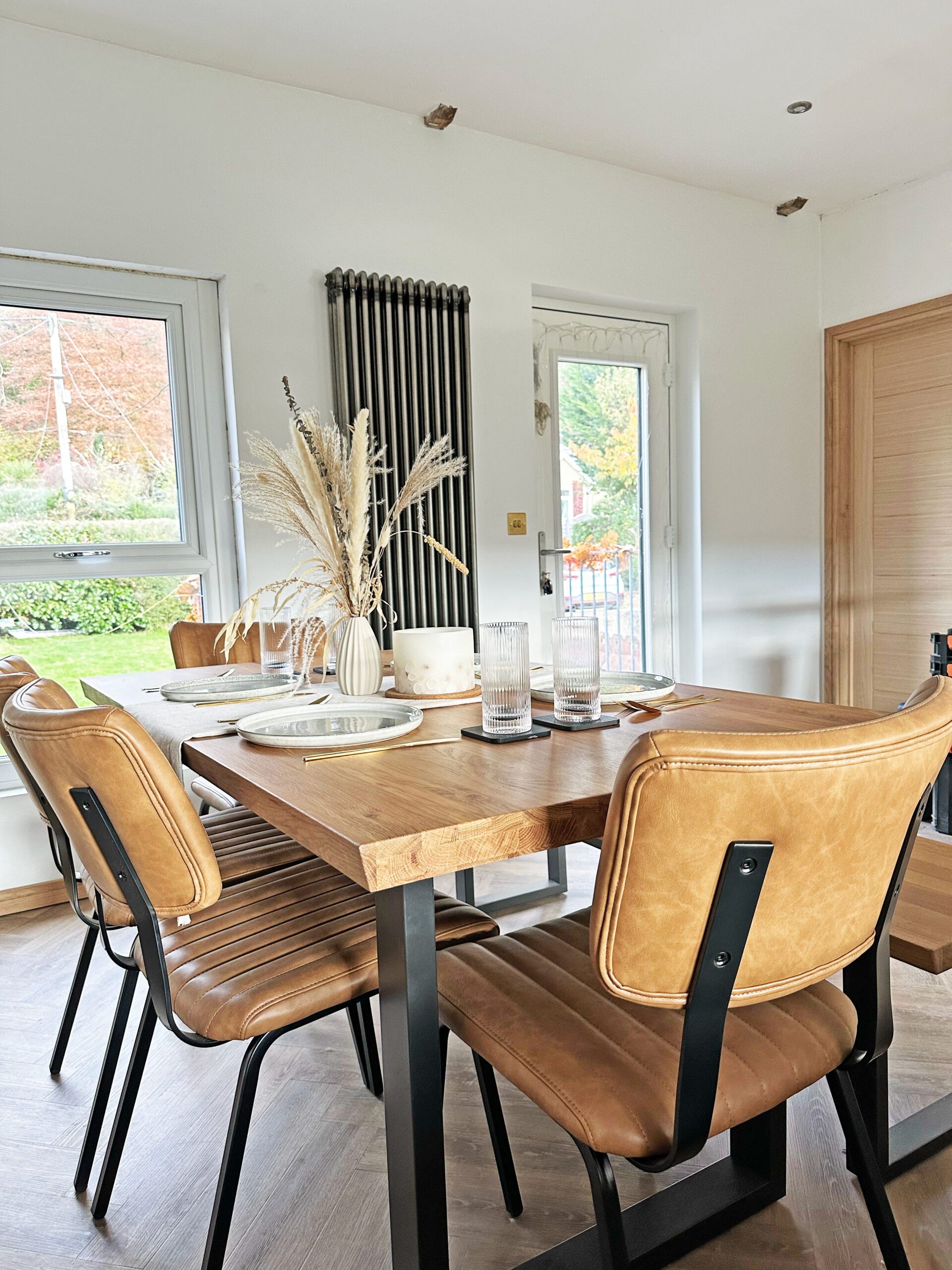 A dining table and chairs-dining room furniture-oak and metal dining table-leather dining chairs-place settings-tablescape-dried flowers-white walls-parquet floor