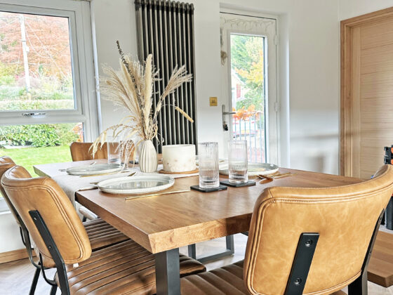 A dining table and chairs-dining room furniture-oak and metal dining table-leather dining chairs-place settings-tablescape-dried flowers-white walls-parquet floor