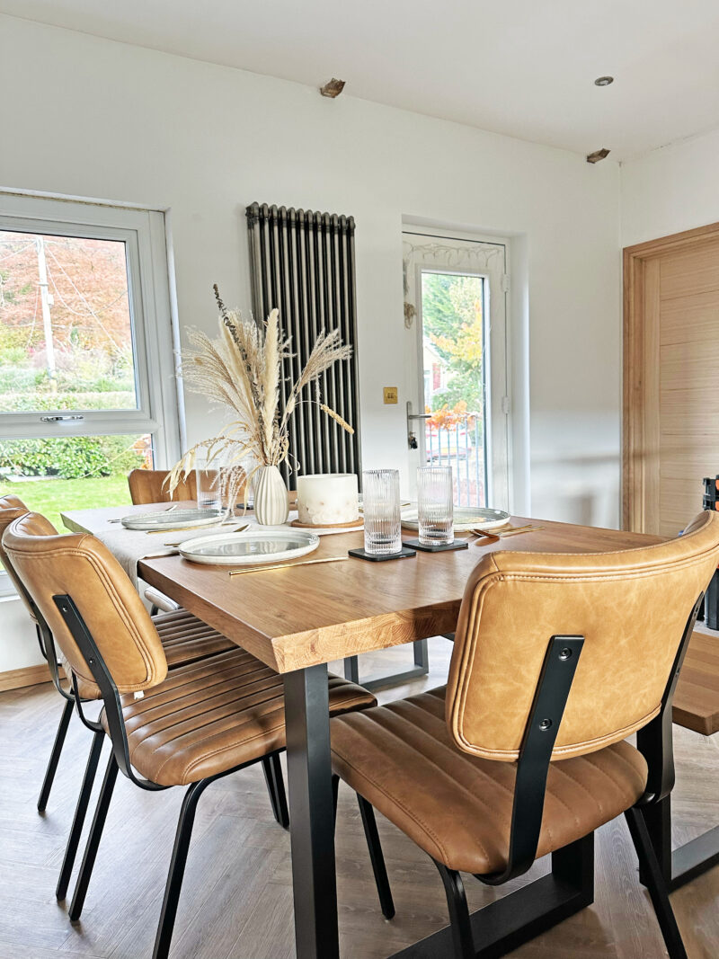 A dining table and chairs-dining room furniture-oak and metal dining table-leather dining chairs-place settings-tablescape-dried flowers-white walls-parquet floor