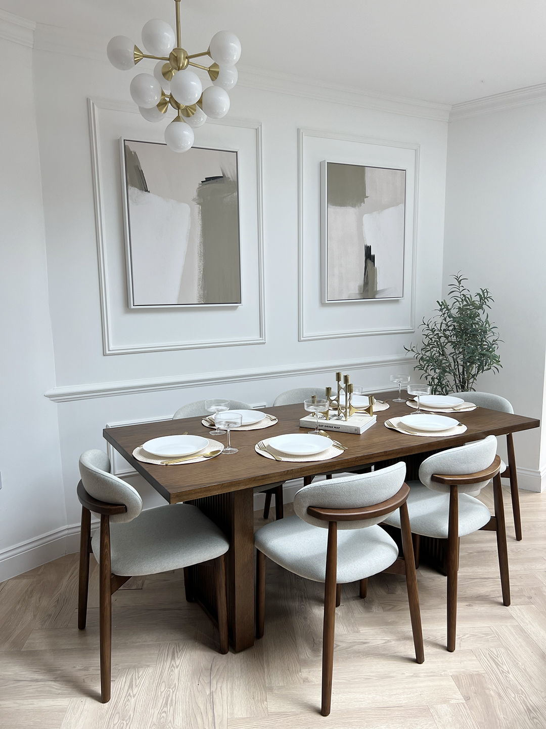 A dining table and chairs-dining room furniture-parquet floor-dark wood dining table-mid century style-dark wood and upholstered dining chairs-wall beading-neutral walls-abstract artwork-statement ceiling light-house plant-table place settings
