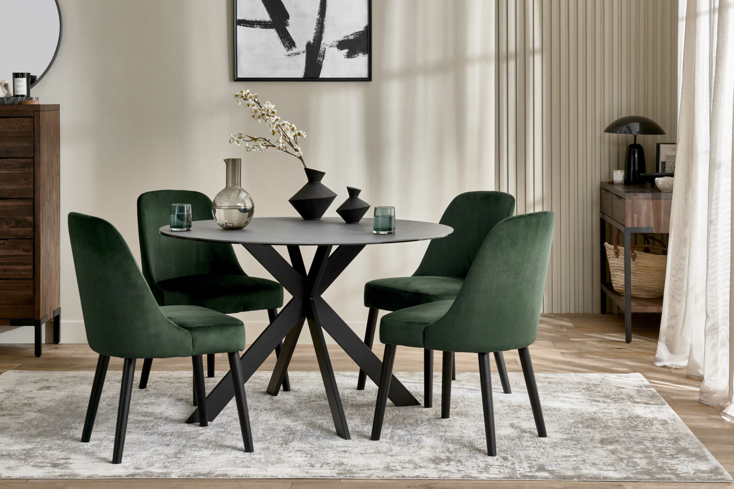 A dining table and chairs-dining room furniture-ceramic table-green upholstered dining chairs-dark wood cabinetry-neutral rug-warm neutral walls-abstract artwork