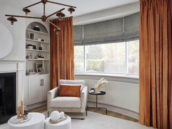 A chair, coffee table and fireplace-living room furniture-orange velvet curtains-grey blinds-statement ceiling light-arched alcove-round plinth coffee tables-off white walls