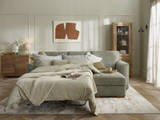 A sofa bed-living room furniture-green corner chaise sofa bed-green striped bedding-neutral knitted throw-beaded walls-wooden tray-glass lamp-mango wood sideboard-display cabinet-abstract wall art-neutral rug-parquet floor-sheer curtain
