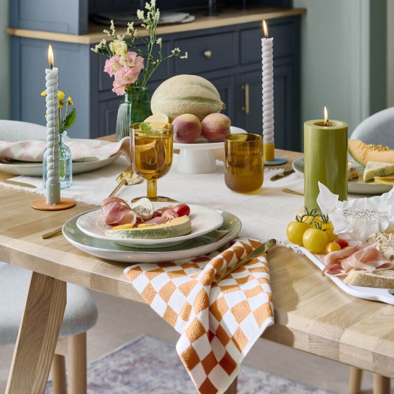 A dining table, chairs, and dresser-dining room furniture-vintage patterned rug-pale oak dining table-upholstered dining chairs-large blue dresser-colourful tablescape-fruit-checkerboard napkins-twisted candles-neutral table runner-fresh flowers