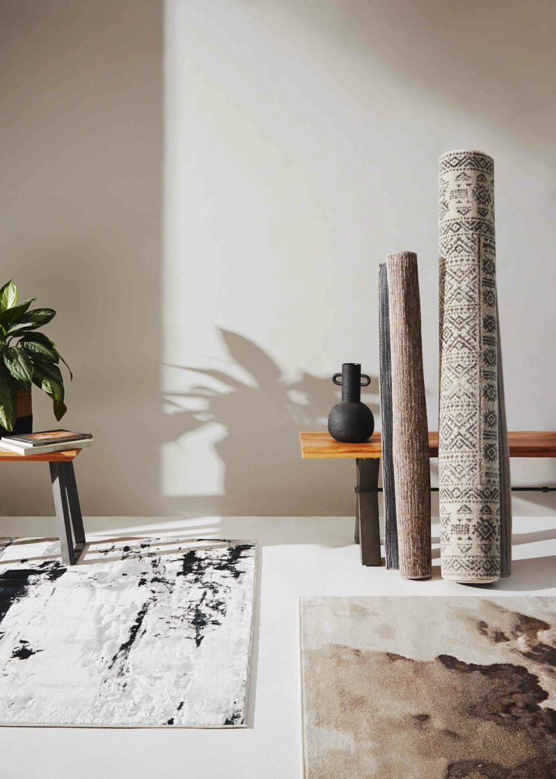 Two neutral rugs on the floor, with two others rolled up resting next to a bench.